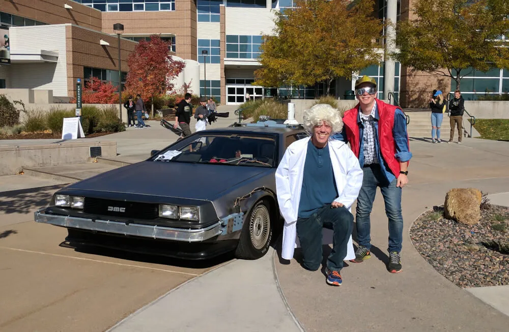 Students cosplaying Doc Brown and Marty McFly with a Delorean in the background.